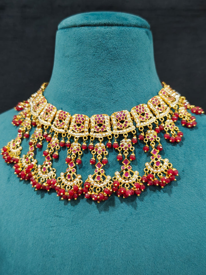 Close-up of an ornate traditional Ruby Pink jadau gold jewellery set and jadau earrings with Beads and gemstones. Close-up of a luxury Jadau imitation necklace styled with a bridal lehenga .Statement Jadau necklace styled for a wedding guest outfit.