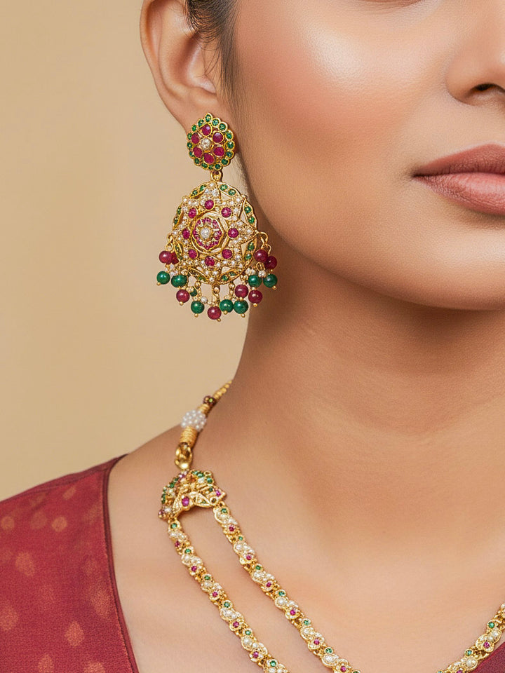 Close-up of a woman wearing an ornate traditional Collar jadau gold jewellery set and jadau earrings with Beads and Pink & Green Colored Stones. Woman wearing a royal Jadau necklace for festive events in India. Festive celebration look featuring a Jadau artificial necklace.