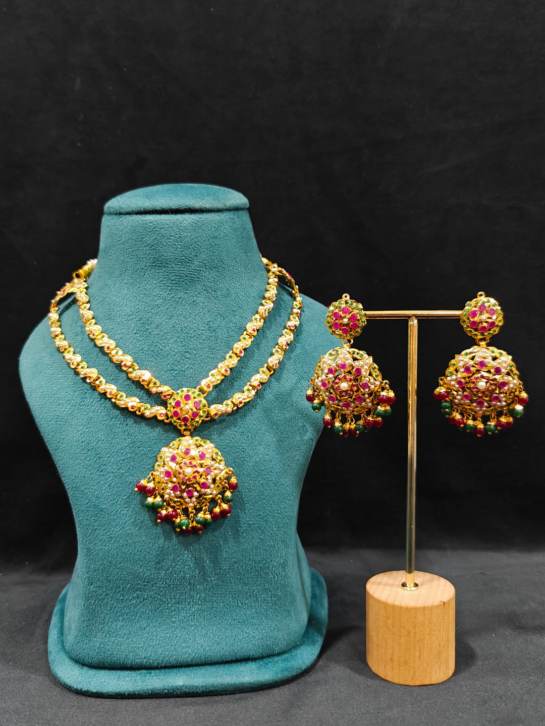 Close-up of an ornate traditional Collar jadau gold jewellery set and jadau earrings with Beads and Pink & Green Colored Stones. Festive celebration look featuring a Jadau artificial necklace. Close-up of intricate Jadau detailing in artificial jewelry.