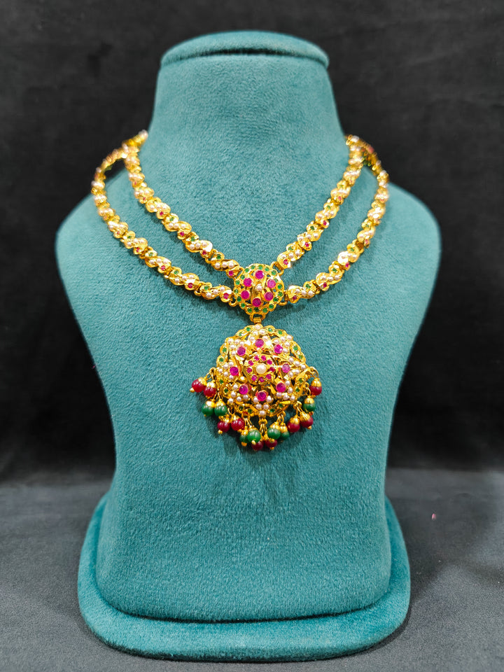 Close-up of an ornate traditional Collar jadau gold jewellery set and jadau earrings with Beads and Pink & Green Colored Stones. Festive celebration look featuring a Jadau artificial necklace. Close-up of intricate Jadau detailing in artificial jewelry.