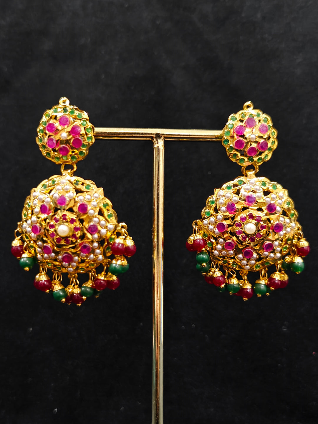 Close-up of an ornate traditional Collar jadau gold jewellery set and jadau earrings with Beads and Pink & Green Colored Stones. Festive celebration look featuring a Jadau artificial necklace. Close-up of intricate Jadau detailing in artificial jewelry.