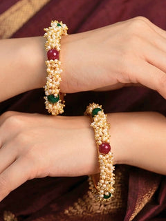 Close-up of a woman wearing an ornate traditional (Gold Polish) White, Red & Green Bangles set with Pearls and Colored Stones. Close-up of handcrafted artificial Pearl bangles with detailed design. Festive Navratri outfit paired with stacked imitation Pearl bangles.