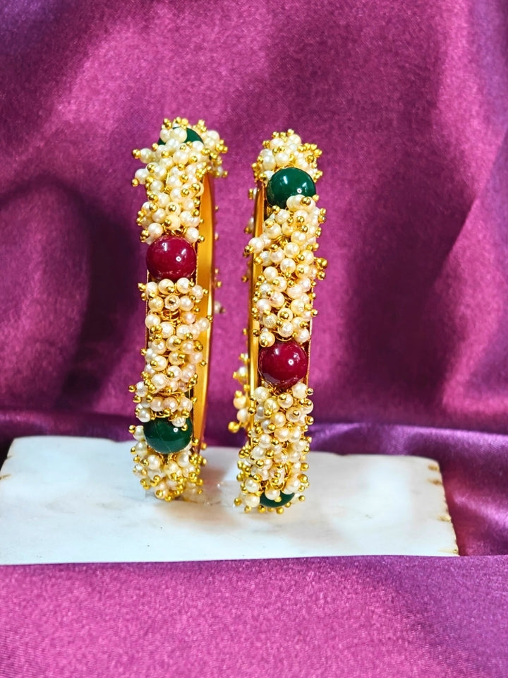 Close-up of a woman wearing an ornate traditional (Gold Polish) White, Red & Green Bangles set with Pearls and Colored Stones. Close-up of handcrafted artificial Pearl bangles with detailed design. Festive Navratri outfit paired with stacked imitation Pearl bangles.