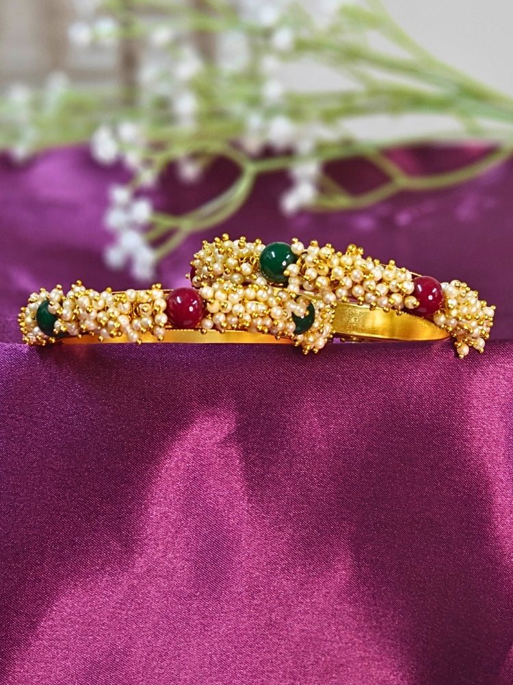 Close-up of a woman wearing an ornate traditional (Gold Polish) White, Red & Green Bangles set with Pearls and Colored Stones. Close-up of handcrafted artificial Pearl bangles with detailed design. Festive Navratri outfit paired with stacked imitation Pearl bangles.