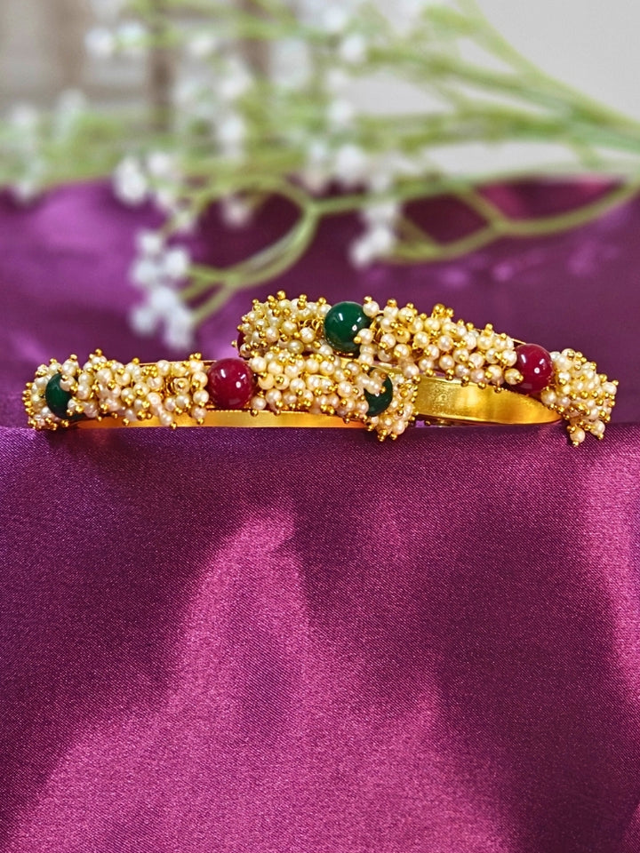 Close-up of a woman wearing an ornate traditional (Gold Polish) White, Red & Green Bangles set with Pearls and Colored Stones. Close-up of handcrafted artificial Pearl bangles with detailed design. Festive Navratri outfit paired with stacked imitation Pearl bangles.
