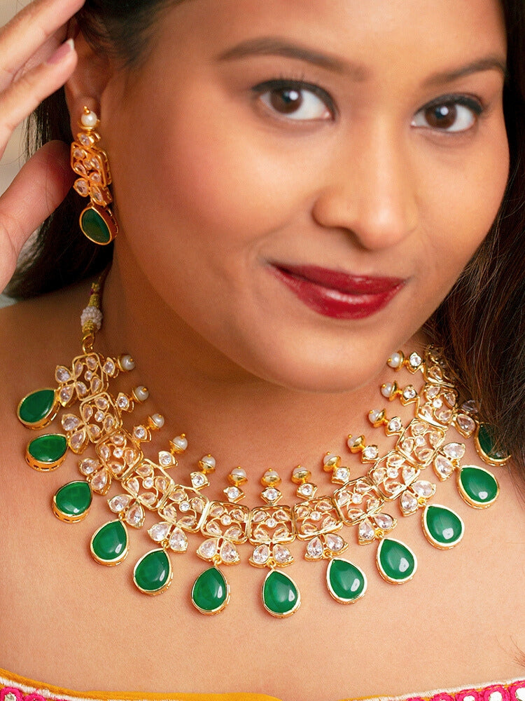 Close-up of a woman wearing an ornate traditional (Gold Polish) Dark Green Collar jewellery set and earrings with Diamond Polki, Monalisa Stone and Colored Stones. Wedding guest wearing a sparkling American diamond necklace with a saree. A graceful woman wearing a trending American diamond necklace for a 2026 wedding celebration.
