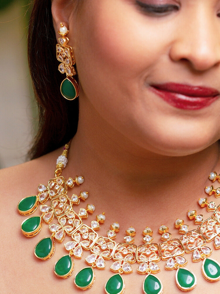 Close-up of a woman wearing an ornate traditional (Gold Polish) Dark Green Collar jewellery set and earrings with Diamond Polki, Monalisa Stone and Colored Stones. Wedding guest wearing a sparkling American diamond necklace with a saree. A graceful woman wearing a trending American diamond necklace for a 2026 wedding celebration.
