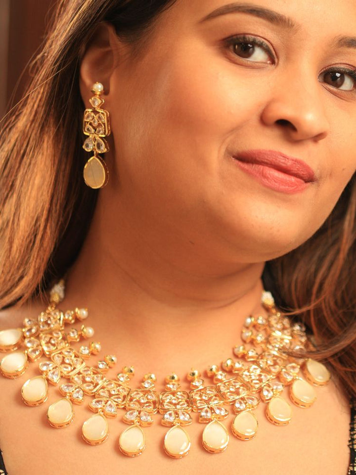 A woman radiates traditional elegance wearing the Rani Kundan Necklace Set with Ivory stones, complete with matching earrings. She smiles softly in an ornate, embroidered outfit accented by mirror embellishments.