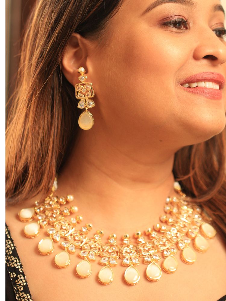 A woman radiates traditional elegance wearing the Rani Kundan Necklace Set with Ivory stones, complete with matching earrings. She smiles softly in an ornate, embroidered outfit accented by mirror embellishments.