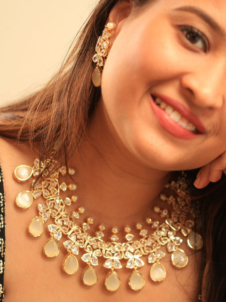 A woman radiates traditional elegance wearing the Rani Kundan Necklace Set with Ivory stones, complete with matching earrings. She smiles softly in an ornate, embroidered outfit accented by mirror embellishments.