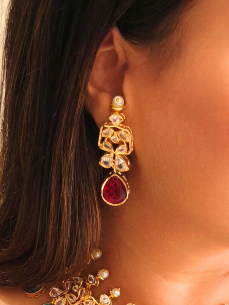 A woman radiates traditional elegance wearing the Rani Kundan Necklace Set with multi-color stones, complete with matching earrings. She smiles softly in an ornate, embroidered outfit accented by mirror embellishments.