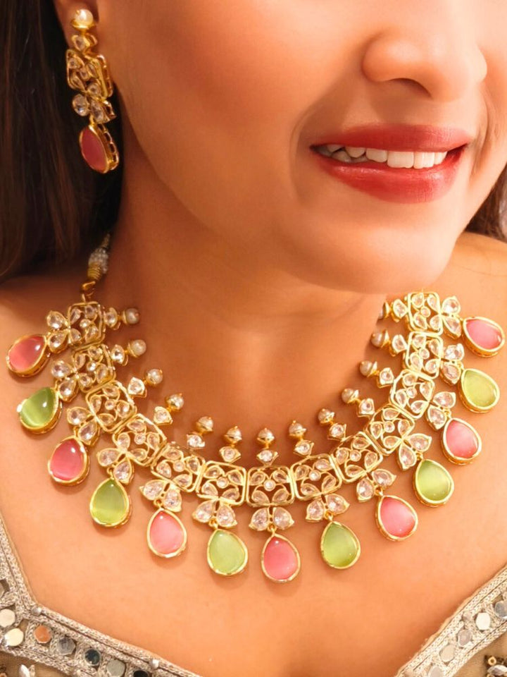 A woman radiates traditional elegance wearing the Rani Kundan Necklace Set with Pink & Green stones, complete with matching earrings. She smiles softly in an ornate, embroidered outfit accented by mirror embellishments.