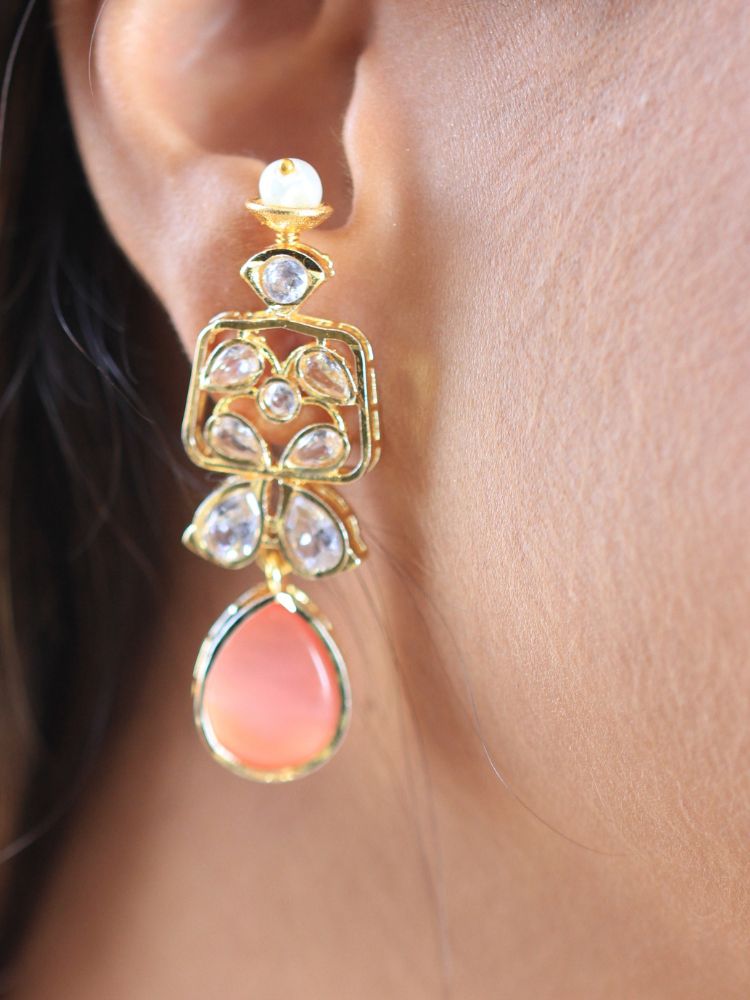 A woman radiates traditional elegance wearing the Rani Kundan Necklace Set with Pink stones, complete with matching earrings. She smiles softly in an ornate, embroidered outfit accented by mirror embellishments.