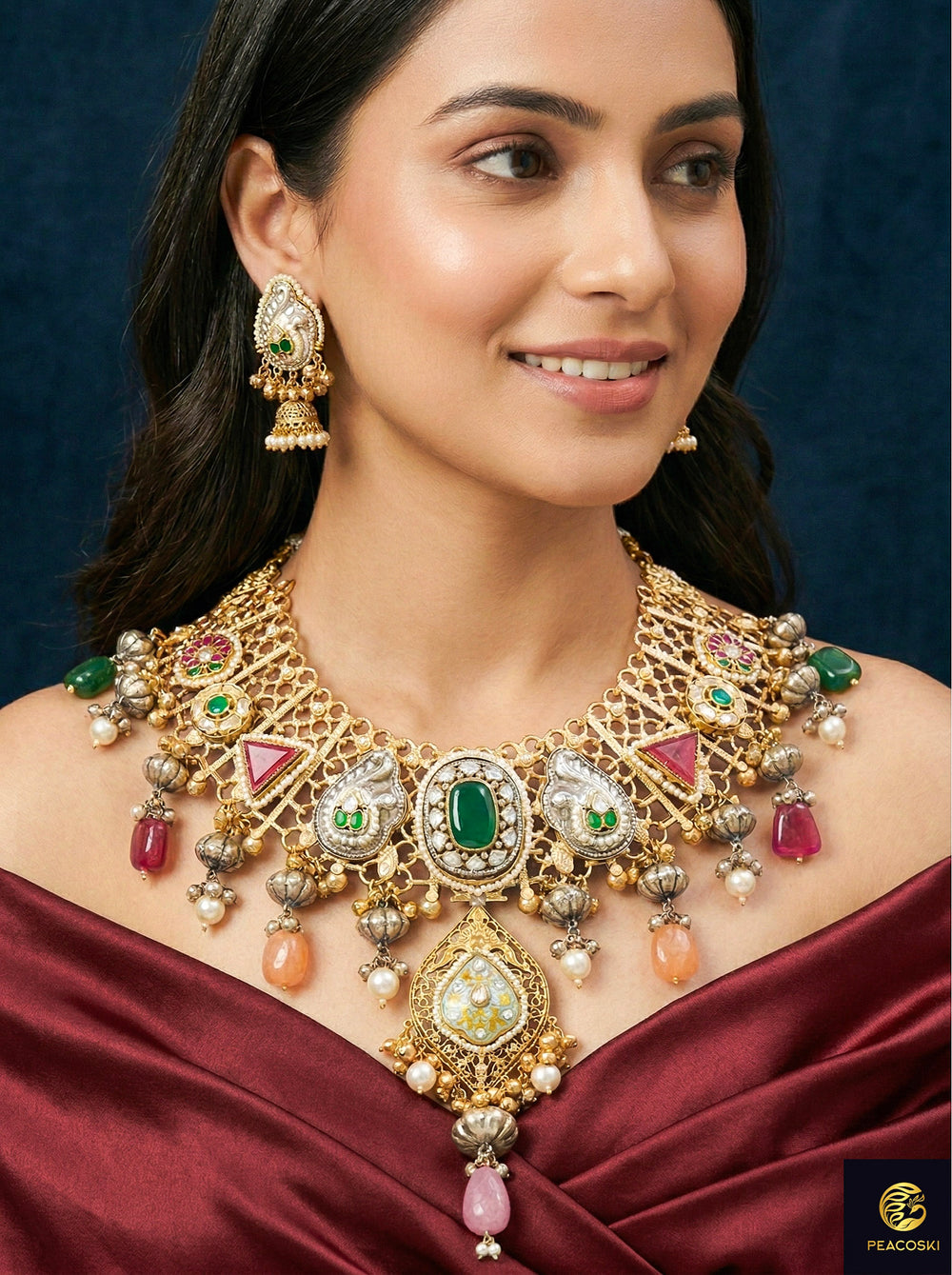Close-up of a woman wearing an ornate traditional KASHMIRI-BOHO Colored Stone Green and Ruby Pink gold Collar jewellery set and earrings with Pachi Kundan, Silver Balls, Pearls, Doublet Stones, Tumble Stone, Ghungroo and Meenakari. Festive celebration look enhanced with traditional Colored Stones jewelry. 