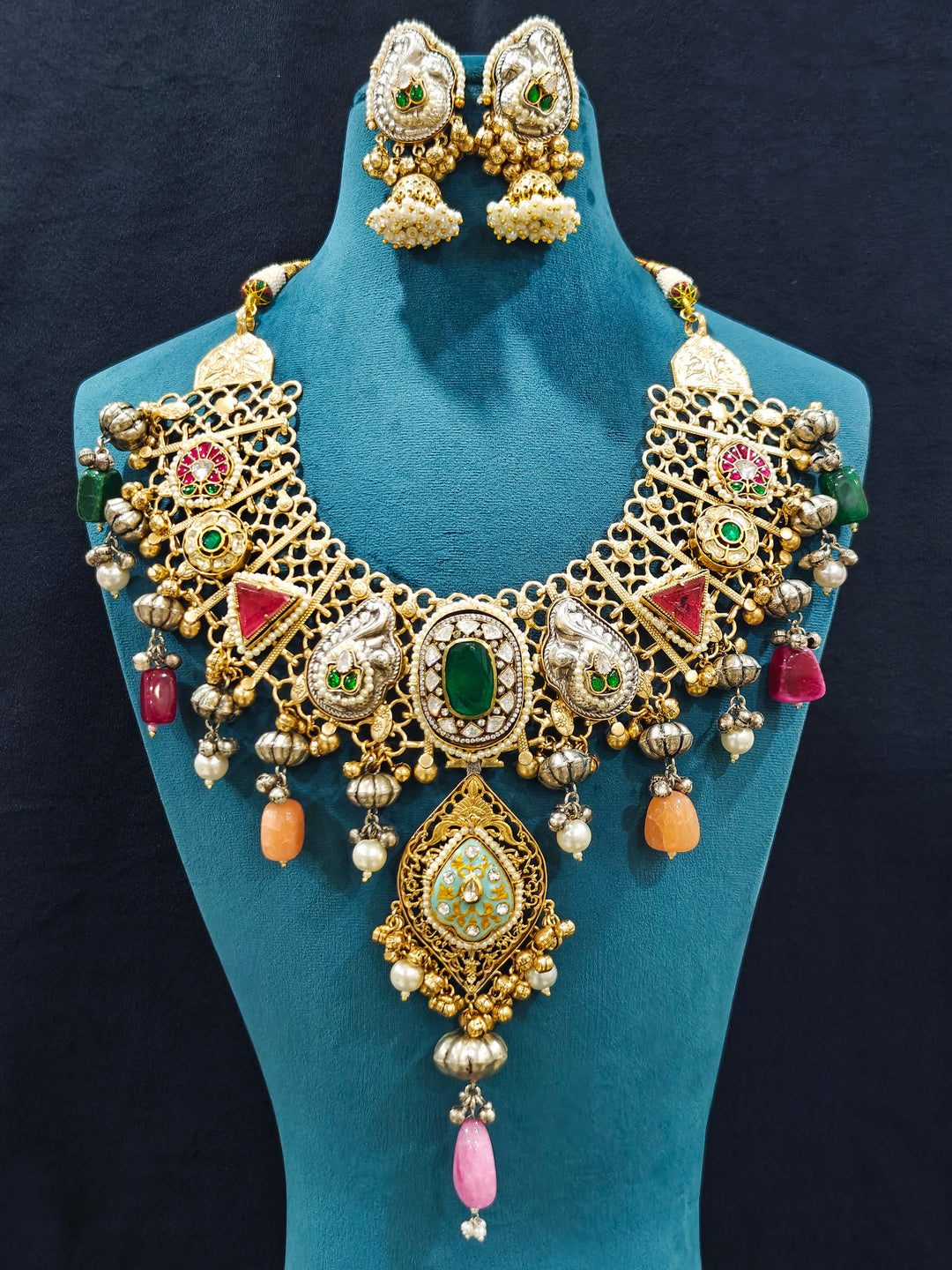Close-up of an ornate traditional KASHMIRI-BOHO Meenakari Green and Ruby Pink gold Collar jewellery set and earrings with Pachi Kundan, Silver Balls, Pearls, Doublet Stones, Tumble Stone, Ghungroo and Meenakari. Festive celebration look enhanced with traditional Meenakari jewelry. 