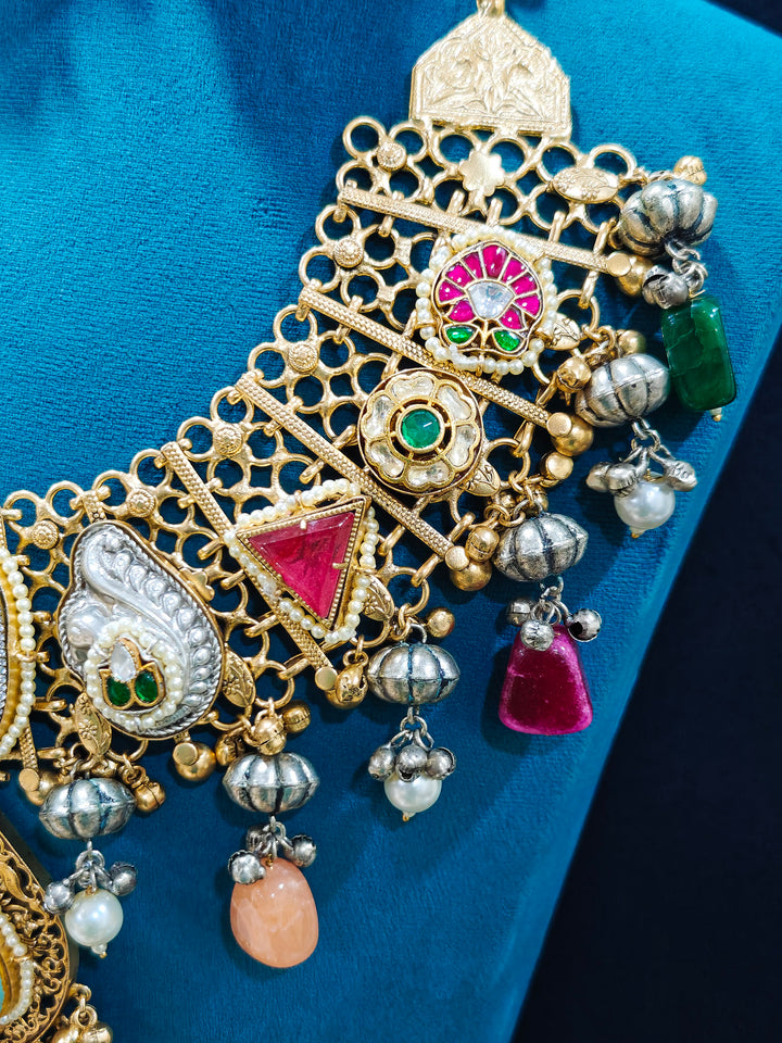 Close-up of an ornate traditional KASHMIRI-BOHO Meenakari Green and Ruby Pink gold Collar jewellery set and earrings with Pachi Kundan, Silver Balls, Pearls, Doublet Stones, Tumble Stone, Ghungroo and Meenakari. Festive celebration look enhanced with traditional Meenakari jewelry. 