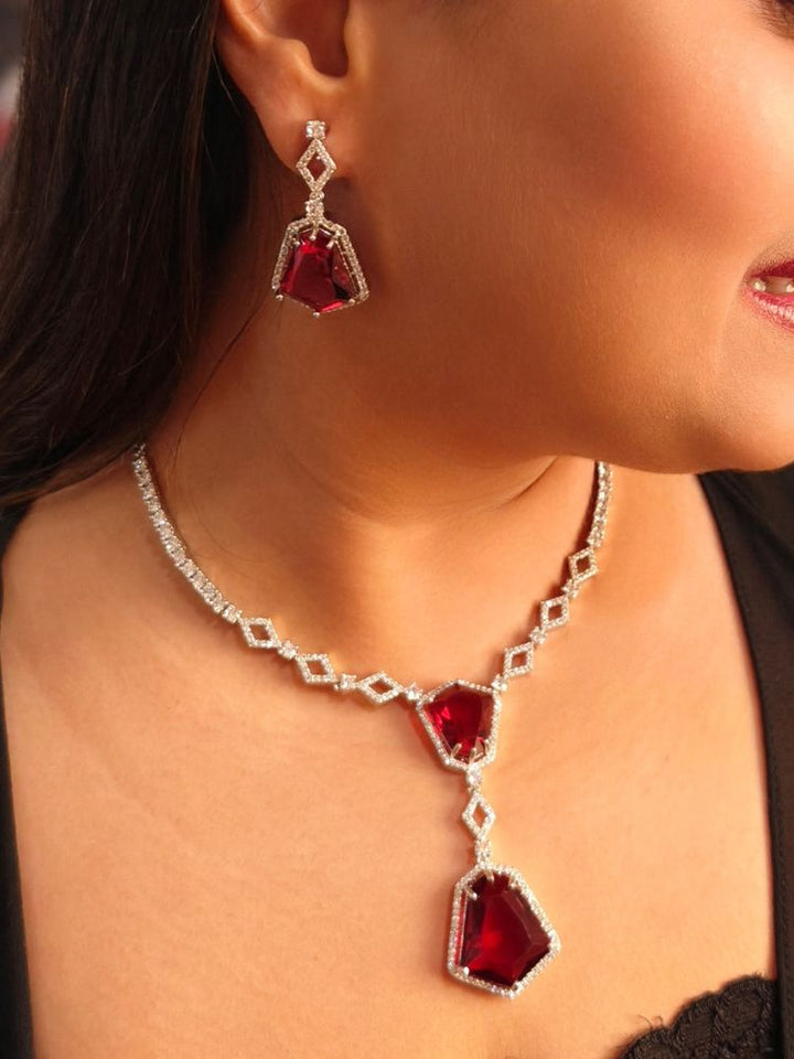 A woman showcases the Angela Red Necklace Set, featuring matching jewelry with bold Red stones and sparkling American Diamonds on both drop earrings and a geometric pendant necklace for a striking look.