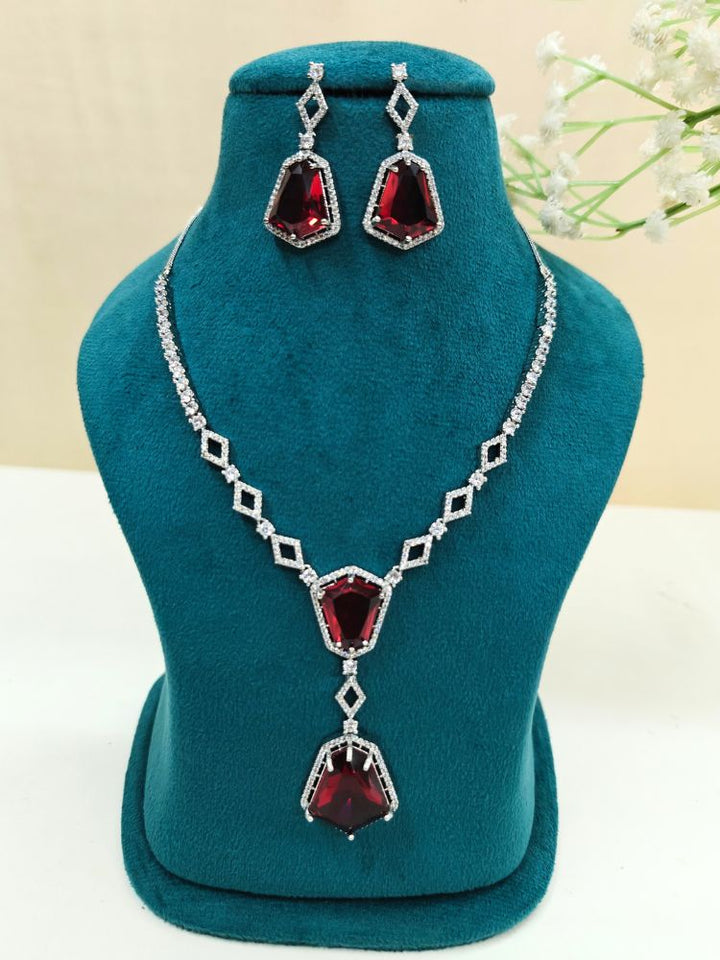 Angela Red Necklace Set, featuring matching jewelry with bold Red stones and sparkling American Diamonds on both drop earrings and a geometric pendant necklace for a striking look. Set on a blue dummy. 