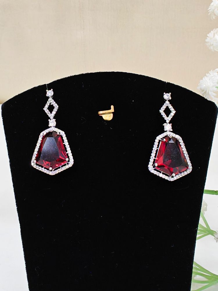A woman showcases the Angela Red Necklace Set, featuring matching jewelry with bold Red stones and sparkling American Diamonds on both drop earrings and a geometric pendant necklace for a striking look. set on a black dummy. 