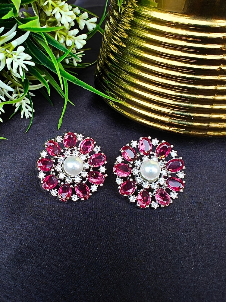 The Red Blossom Earrings showcase a central white pearl encircled by alternating Red stones and American diamonds, elegantly displayed on Black fabric with green leaves and a Golden accent.