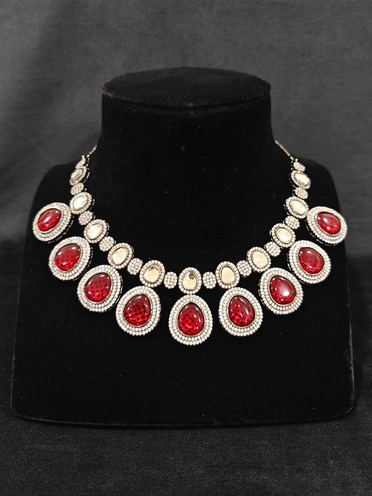 Close-up of an ornate Indo-western American Diamond Red Collar jewellery set and earrings with American Diamonds and Monalisa Stones. Woman styling a statement American diamond necklace with an off-shoulder gown for a reception. Close-up of a luxury American Diamond imitation necklace styled.