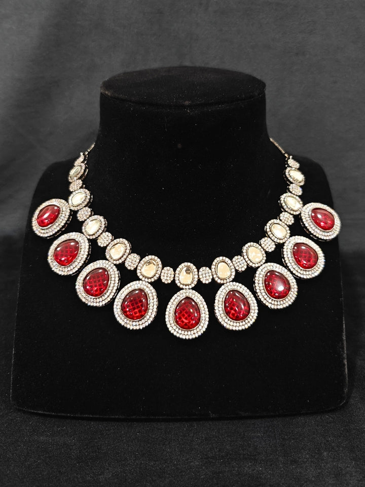 Close-up of an ornate Indo-western American Diamond Red Collar jewellery set and earrings with American Diamonds and Monalisa Stones. Woman styling a statement American diamond necklace with an off-shoulder gown for a reception. Close-up of a luxury American Diamond imitation necklace styled.