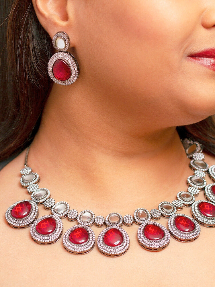 A woman with brown hair down smiles to the side, wearing the Red Elizabeth Necklace Set featuring a statement Victorian-style necklace and matching earrings with large colorful stones, paired with a sparkly dark top.