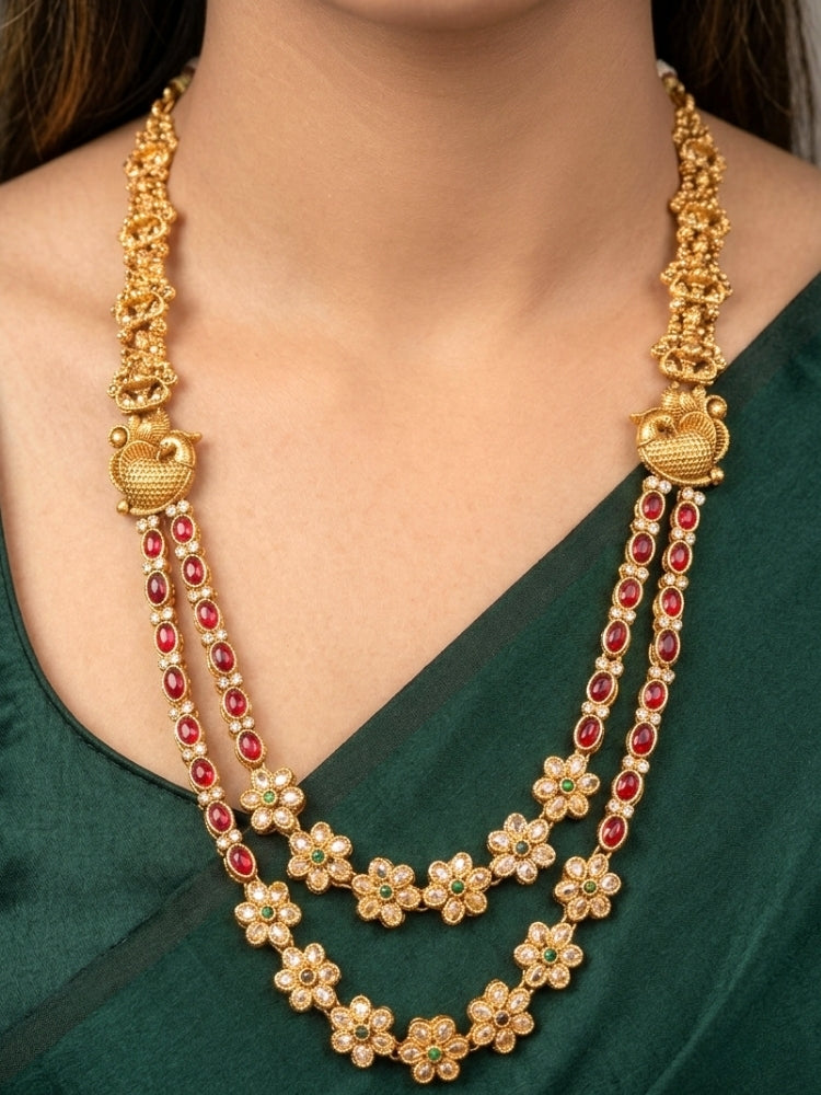 A woman wearing the Red & Green Karuna Temple Necklace Set featuring a traditional gold Long necklace and matching earrings with Red and green colored stones, paired with a Saree—Saree look enhanced with a royal temple imitation necklace.
