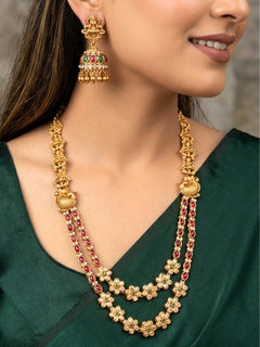 A woman wearing the Red & Green Karuna Temple Necklace Set featuring a traditional gold Long necklace and matching earrings with Red and green colored stones, paired with a Saree—Saree look enhanced with a royal temple imitation necklace.