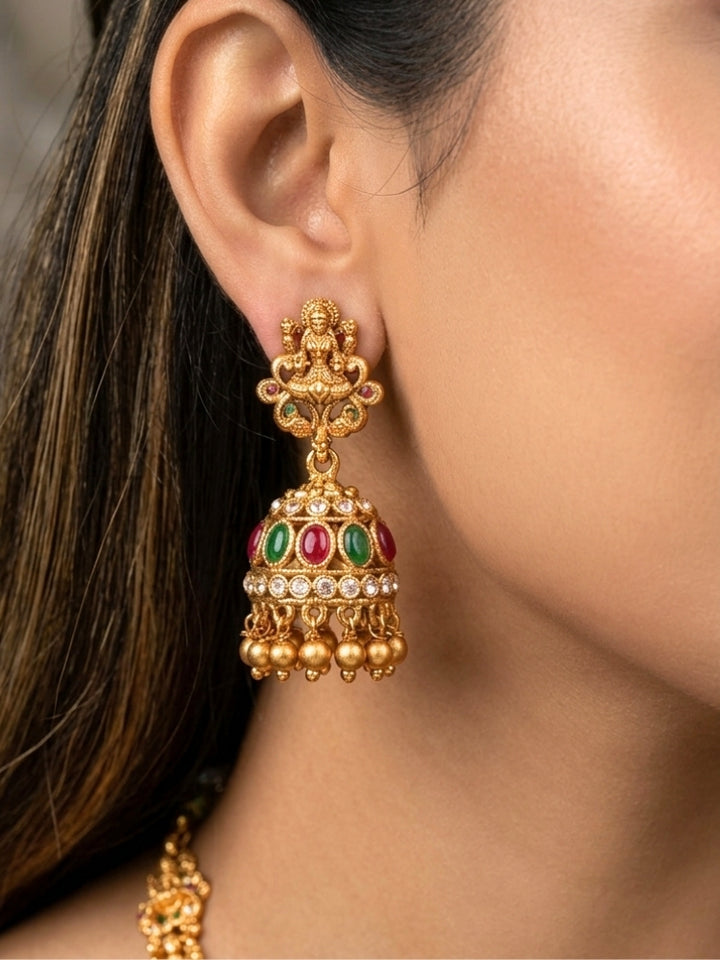 A woman wearing the Red & Green Karuna Temple Necklace Set featuring a traditional gold Long necklace and matching earrings with Red and green colored stones, paired with a Saree—Saree look enhanced with a royal temple imitation necklace.