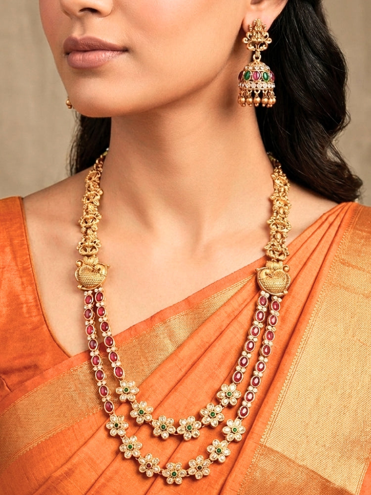 A woman wearing the Red & Green Karuna Temple Necklace Set featuring a traditional gold Long necklace and matching earrings with Red and green colored stones, paired with a Saree—Saree look enhanced with a royal temple imitation necklace.