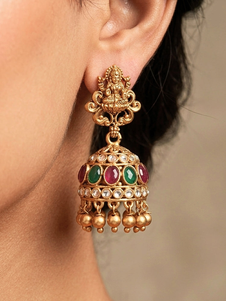 A woman wearing the Red & Green Karuna Temple Necklace Set featuring a traditional gold Long necklace and matching earrings with Red and green colored stones, paired with a Saree—Saree look enhanced with a royal temple imitation necklace.