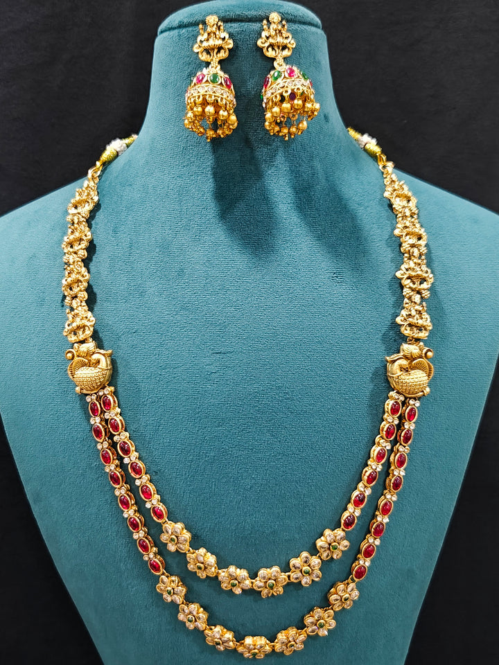 The Red & Green Karuna Temple Necklace Set featuring a traditional gold Long necklace and matching earrings with Red and green colored stones, Close-up of detailed temple carvings in artificial wedding jewelry.