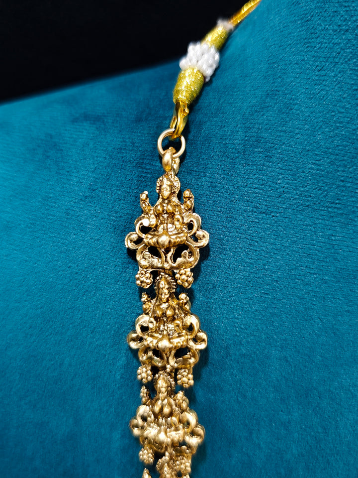 The Red & Green Karuna Temple Necklace Set featuring a traditional gold Long necklace and matching earrings with Red and green colored stones, Close-up of detailed temple carvings in artificial wedding jewelry.