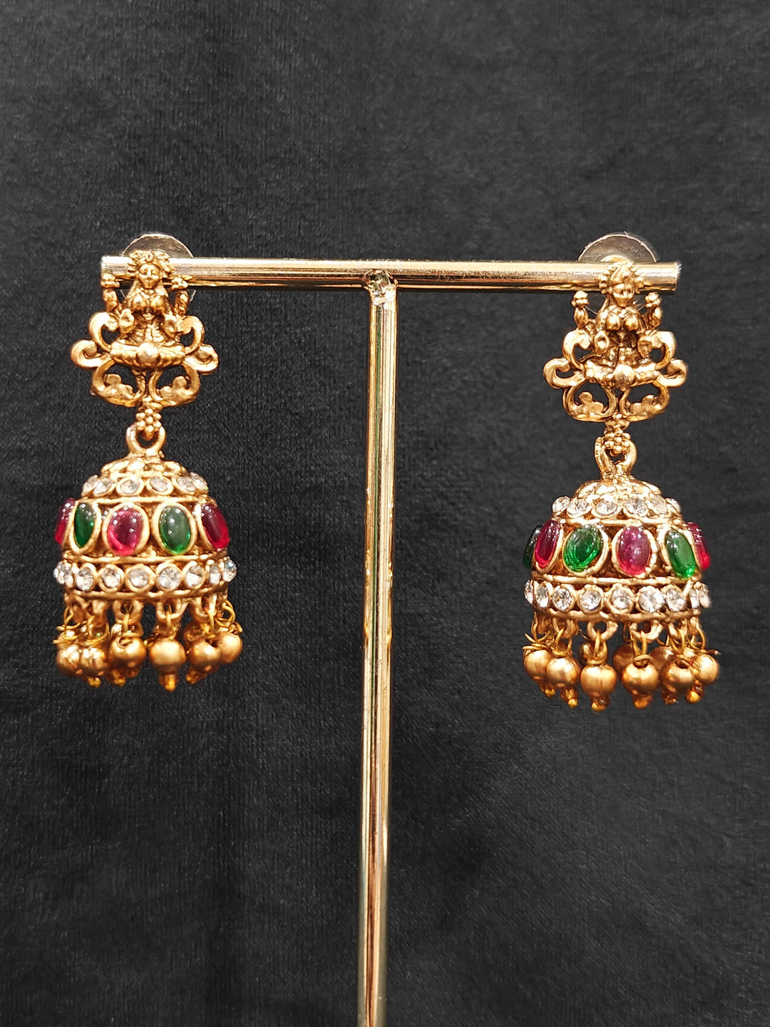 The Red & Green Karuna Temple Necklace Set featuring a traditional gold Long necklace and matching earrings with Red and green colored stones, Close-up of detailed temple carvings in artificial wedding jewelry.