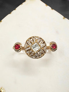 The Red Octavia Ring features a gold band with a round, ornate centerpiece set with a clear American Diamond and two smaller red gemstones on the side, displayed on a white surface with gold trim. Multi-finger ring, great for cocktail parties. 