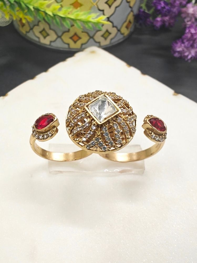The Red Octavia Ring features a gold band with a round, ornate centerpiece set with a clear American Diamond and two smaller red gemstones on the side, displayed on a white surface with gold trim. Multi-finger ring, great for cocktail parties. 