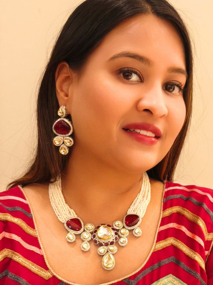 A woman in a Red embroidered outfit smiles, showcasing the Peacoski Red Tamanna Necklace Set and matching earrings. Her soft makeup highlights the elegance of this statement jewelry ensemble.