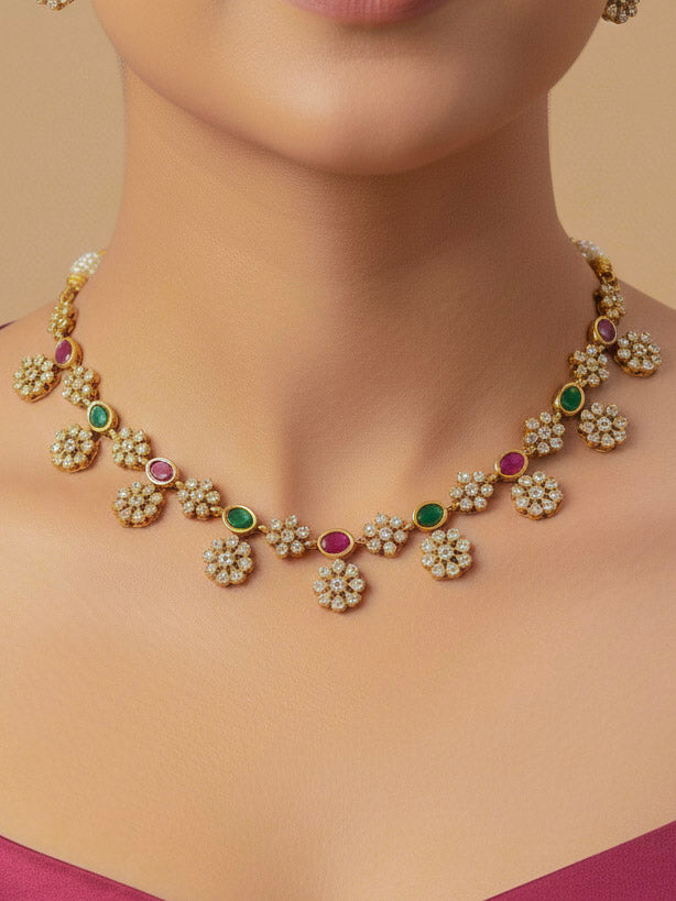 Close-up of a woman wearing an ornate traditional Diamond (gold Polish) Red & Green Collar jewellery set and earrings with American Diamond and Colored Stones. Mehendi function outfit styled with a lightweight American Diamond necklace. 