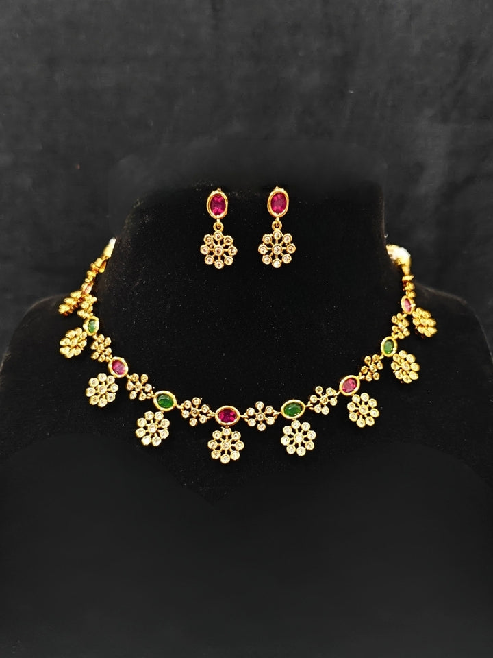 Close-up of an ornate traditional Diamond (gold Polish) Red & Green Collar jewellery set and earrings with American Diamond and Colored Stones. Mehendi function outfit styled with a lightweight American Diamond necklace. 