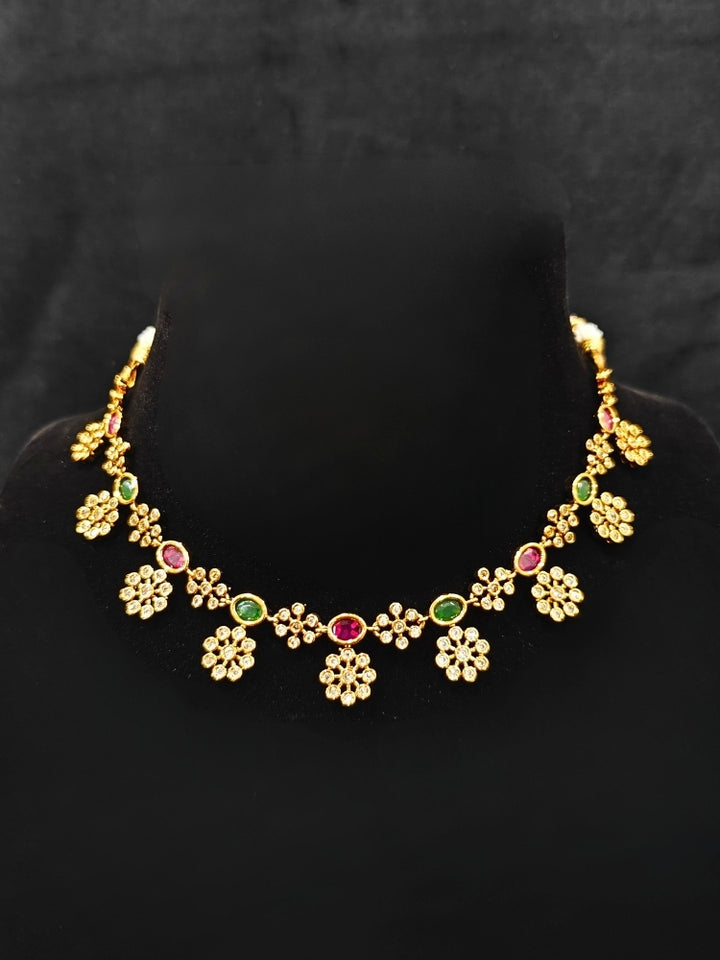 Close-up of a woman wearing an ornate traditional Diamond (gold Polish) Red & Green Collar jewellery set and earrings with American Diamond and Colored Stones. Mehendi function outfit styled with a lightweight American Diamond necklace. 
