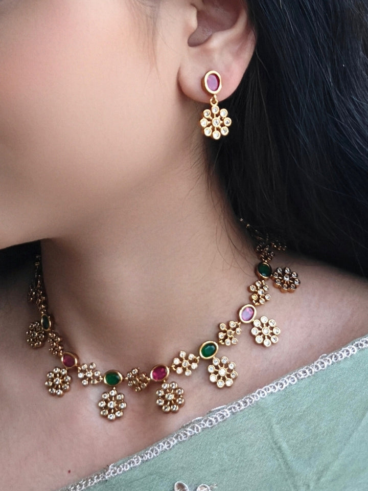 Close-up of a woman wearing an ornate traditional Diamond (gold Polish) Red & Green Collar jewellery set and earrings with American Diamond and Colored Stones. Mehendi function outfit styled with a lightweight American Diamond necklace. 