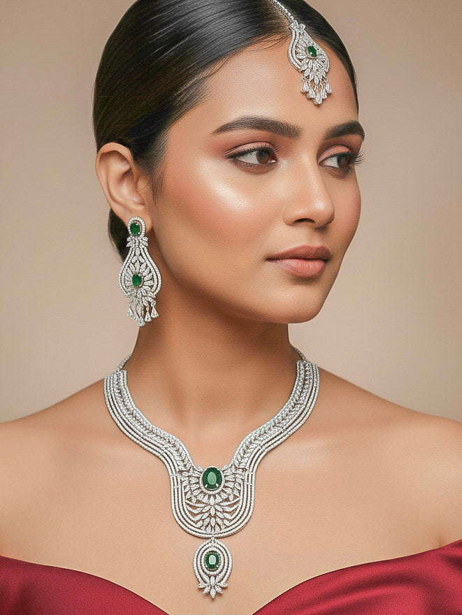 "A stunning woman wearing a glamorous artificial diamond and green colored stone  necklace paired with chic earrings and maangtikka, perfect for bridal wear. This high-quality artificial diamond jewelry set is the ideal choice for modern brides looking for a budget-friendly option with timeless sparkle."
