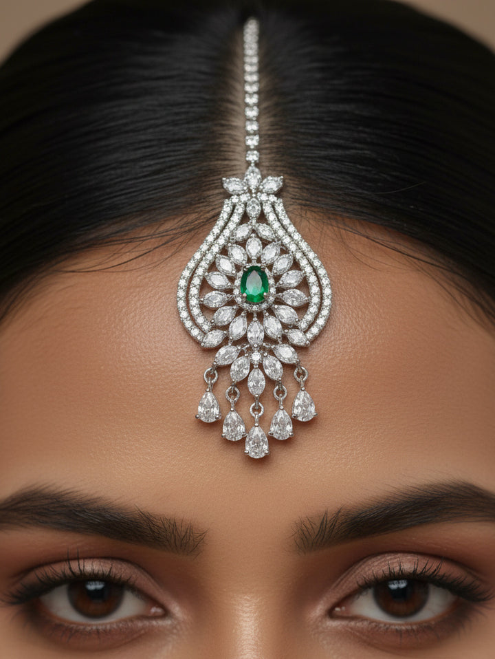 "A woman in a traditional saree, wearing a gorgeous artificial diamond and green colored stone necklace paired with diamond earrings and diamond maangtikka. This artificial diamond jewelry set offers a traditional yet modern touch for Indian brides, designed to add elegance and sophistication to any occasion."

