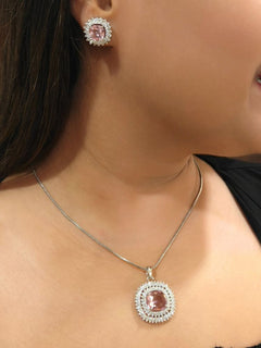 A woman wears the Peacoski Renne Mint Pink Pendant Set, a matching jewelry set with a mint pink pendant necklace and stud earrings featuring large stones surrounded by American Diamonds, all in silver. She pairs it with a black top.
