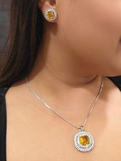 A woman wears the Peacoski Renne Yellow Pendant Set, featuring a yellow pendant necklace and American Diamond stud earrings, perfectly complementing her elegant cocktail gown.