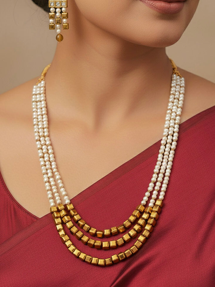 Close-up of a woman wearing an ornate Indo-Western White and Gold Pearl Layered Jewellery set and Earring with Pearls and American Diamond. Festive celebration look enhanced with traditional Pearl jewelry. Close-up of enamel work in Meenakari artificial Pearl jewelry.