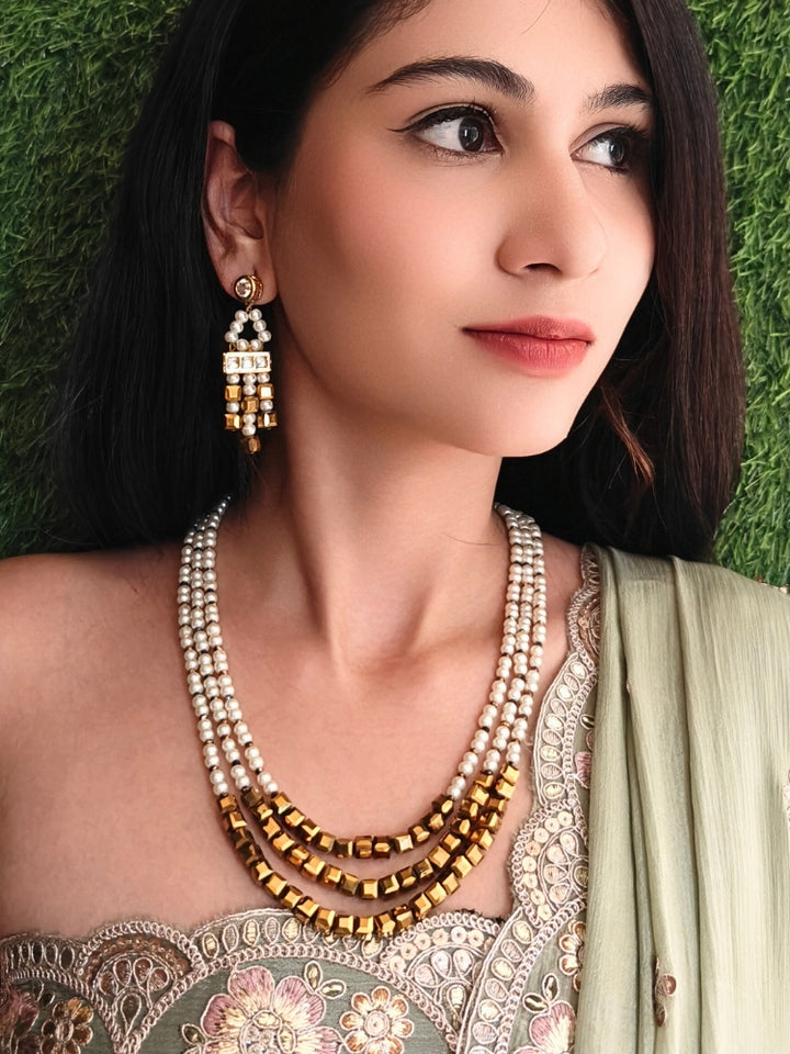 Close-up of a woman wearing an ornate Indo-Western White and Gold Pearl Layered Jewellery set and Earring with Pearls and American Diamond. Festive celebration look enhanced with traditional Pearl jewelry. Close-up of enamel work in Meenakari artificial Pearl jewelry.