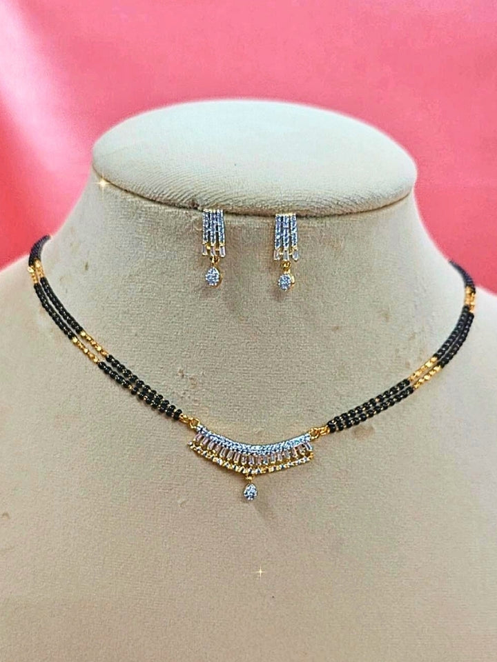 Ritu Mangalsutra—a gold necklace with black mangalsutra beads and matching earrings, pendant featuring sparkling American Diamonds—set against a cream dummy, perfect for your wedding ceremony dress. Diamond mangalsutra. Modern mangalsutra. 
