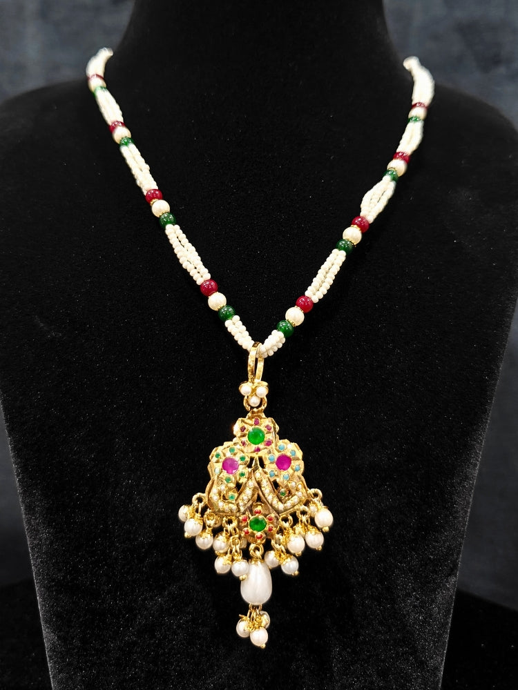 Close-up of an ornate traditional (Gold Polish) Multi-Color Pendant Set and Earrings with  Pearl and Colored Stones. Festive saree look completed with a handcrafted Jadau Pendant. Close-up of high-quality Jadau artificial Pendant craftsmanship.